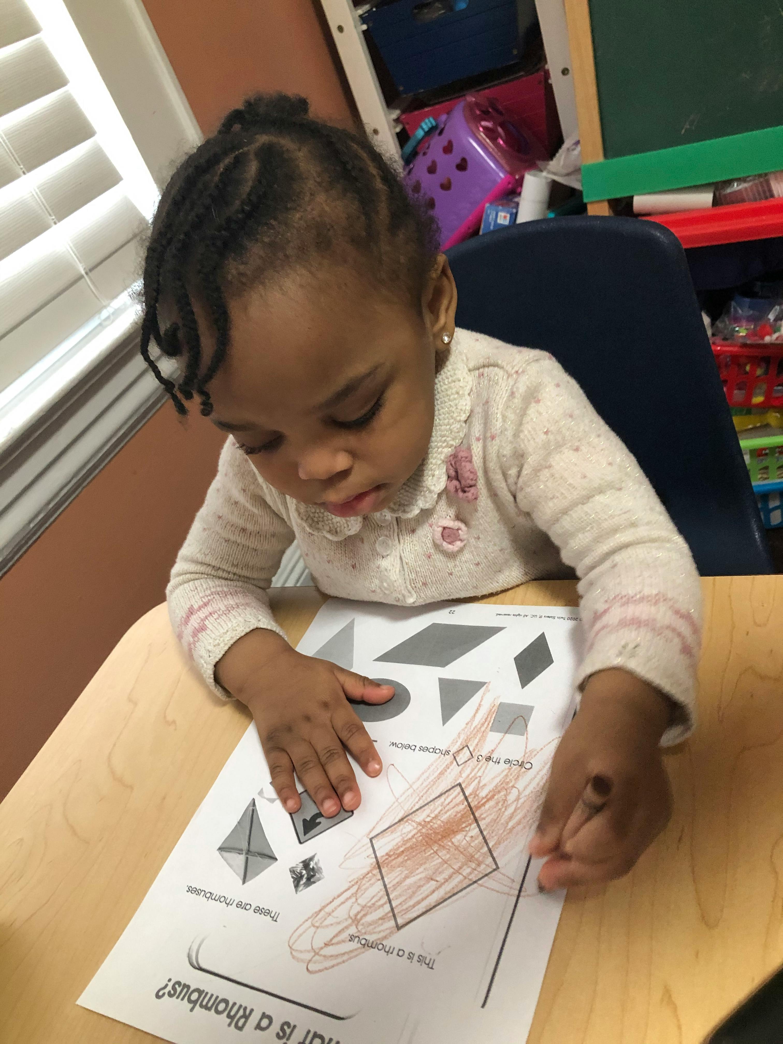 Child coloring a shape on a worksheet at a desk