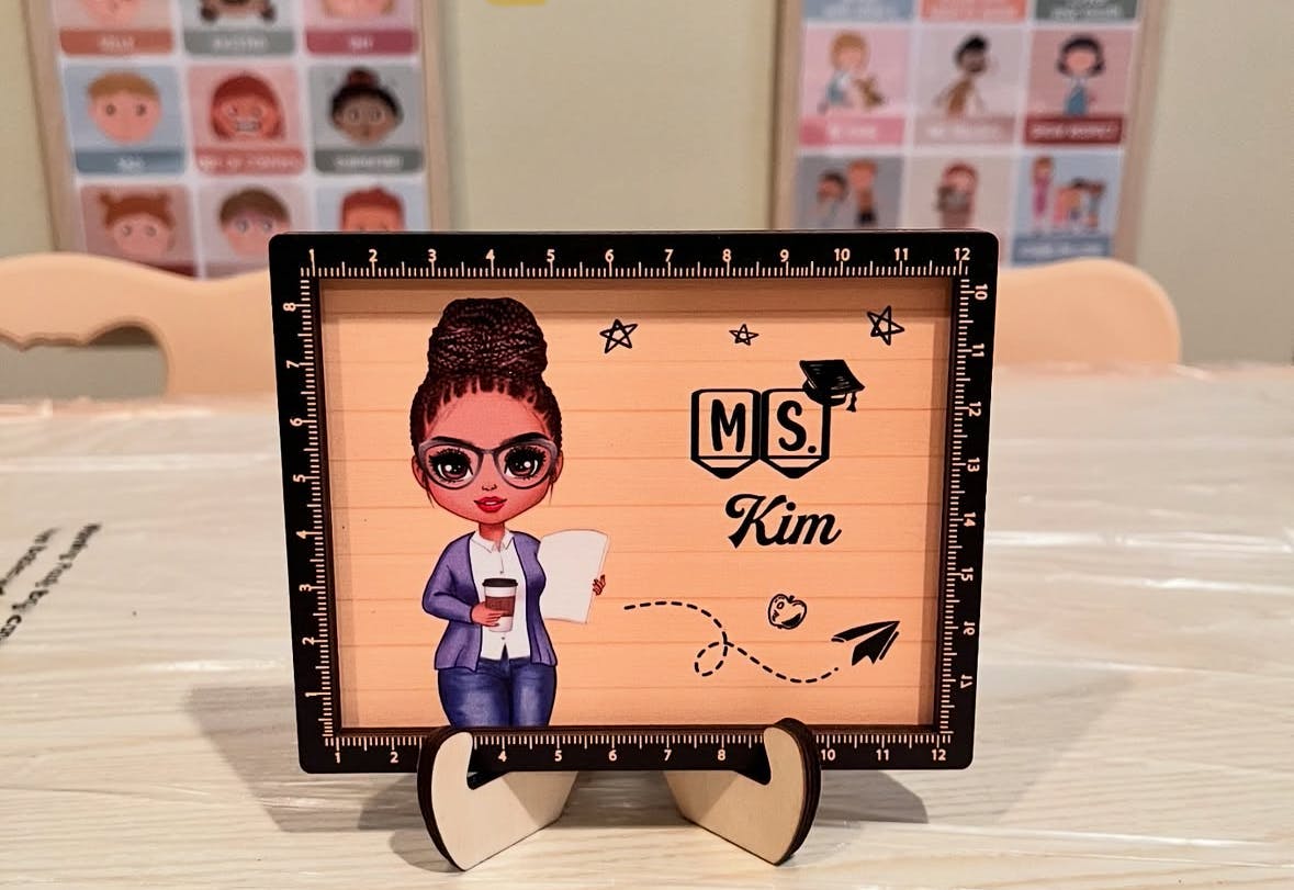 Decorative sign with a cartoon person holding a cup and paper, text "MS. Kim"