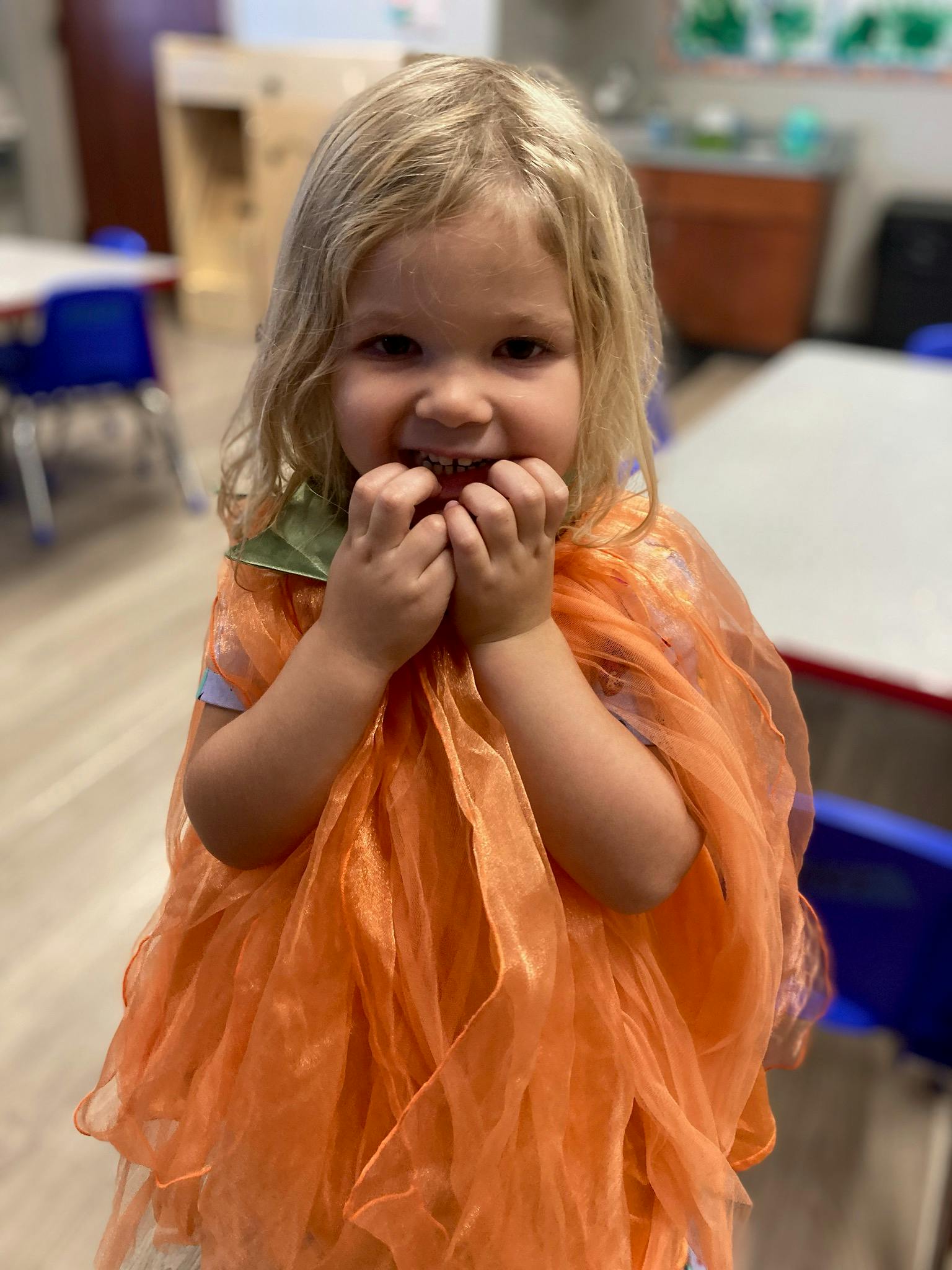 Child in an orange costume with hands near mouth