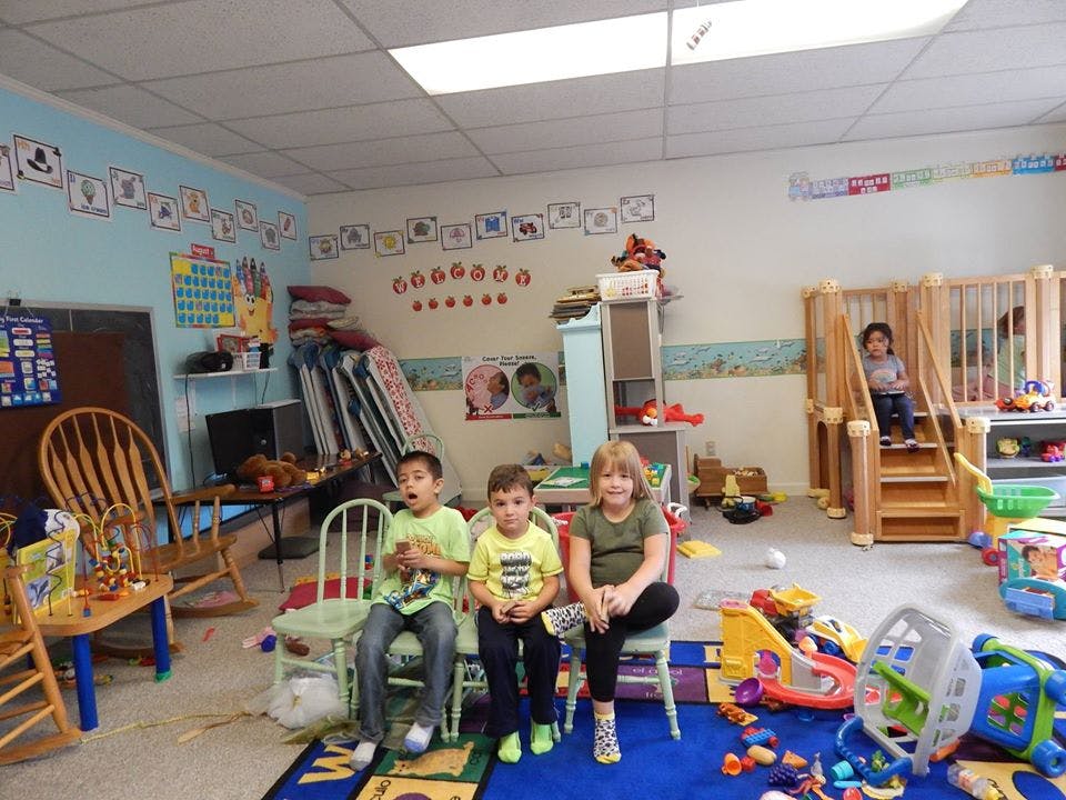 Three children sitting in a classroom with another child on a play structure