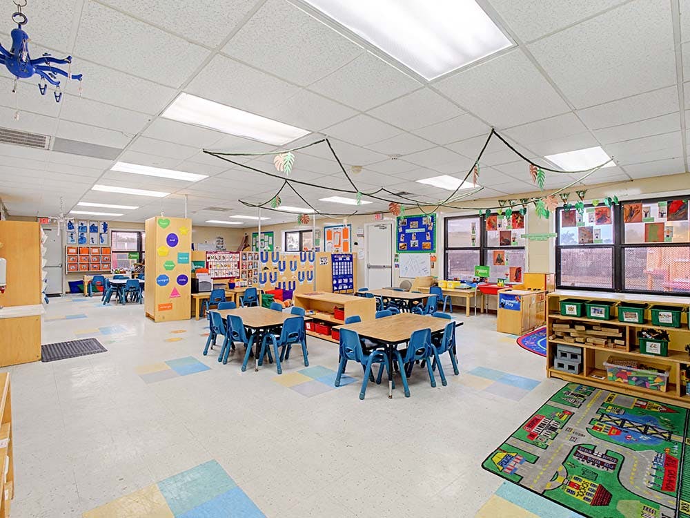 Classroom with small tables and chairs, colorful decorations, and a play rug