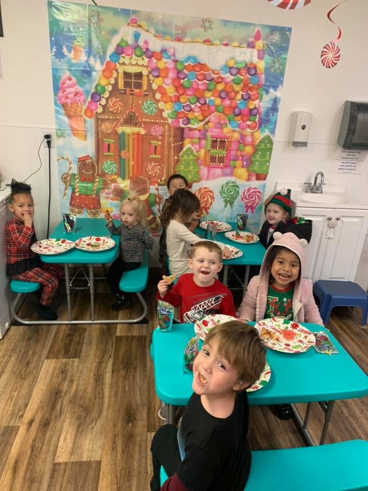 Children sitting at tables with plates in front of a colorful backdrop