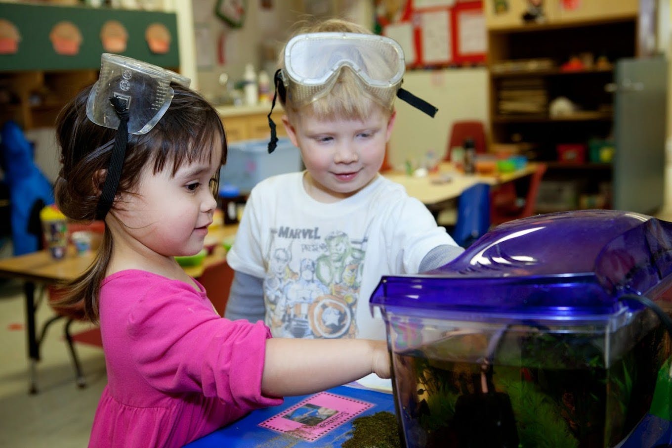 Two children wearing safety goggles looking at a container