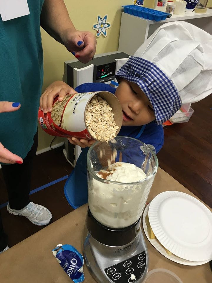 Child in a chef hat pouring oats into a blender