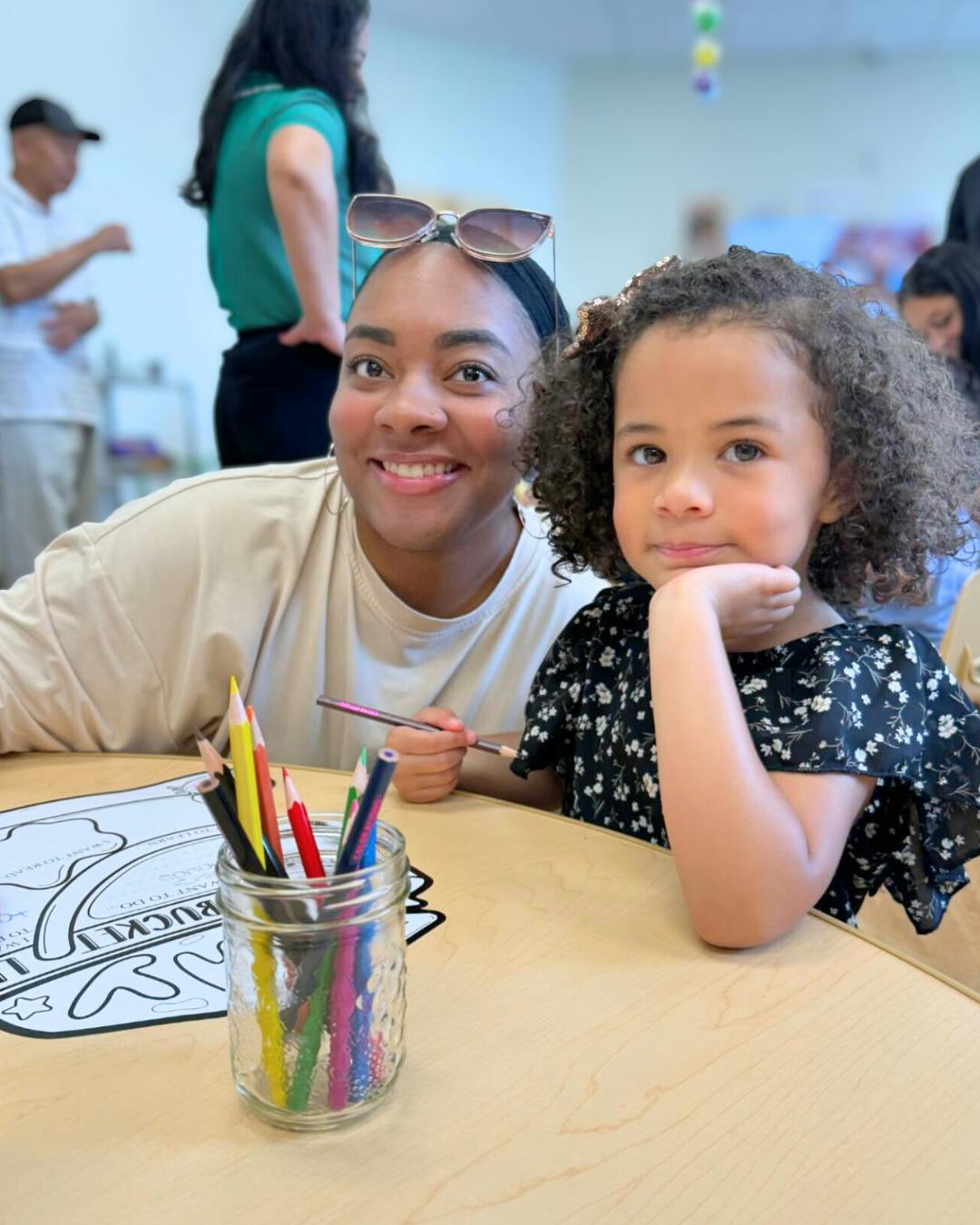 Smiling person and child coloring at a table with crayons