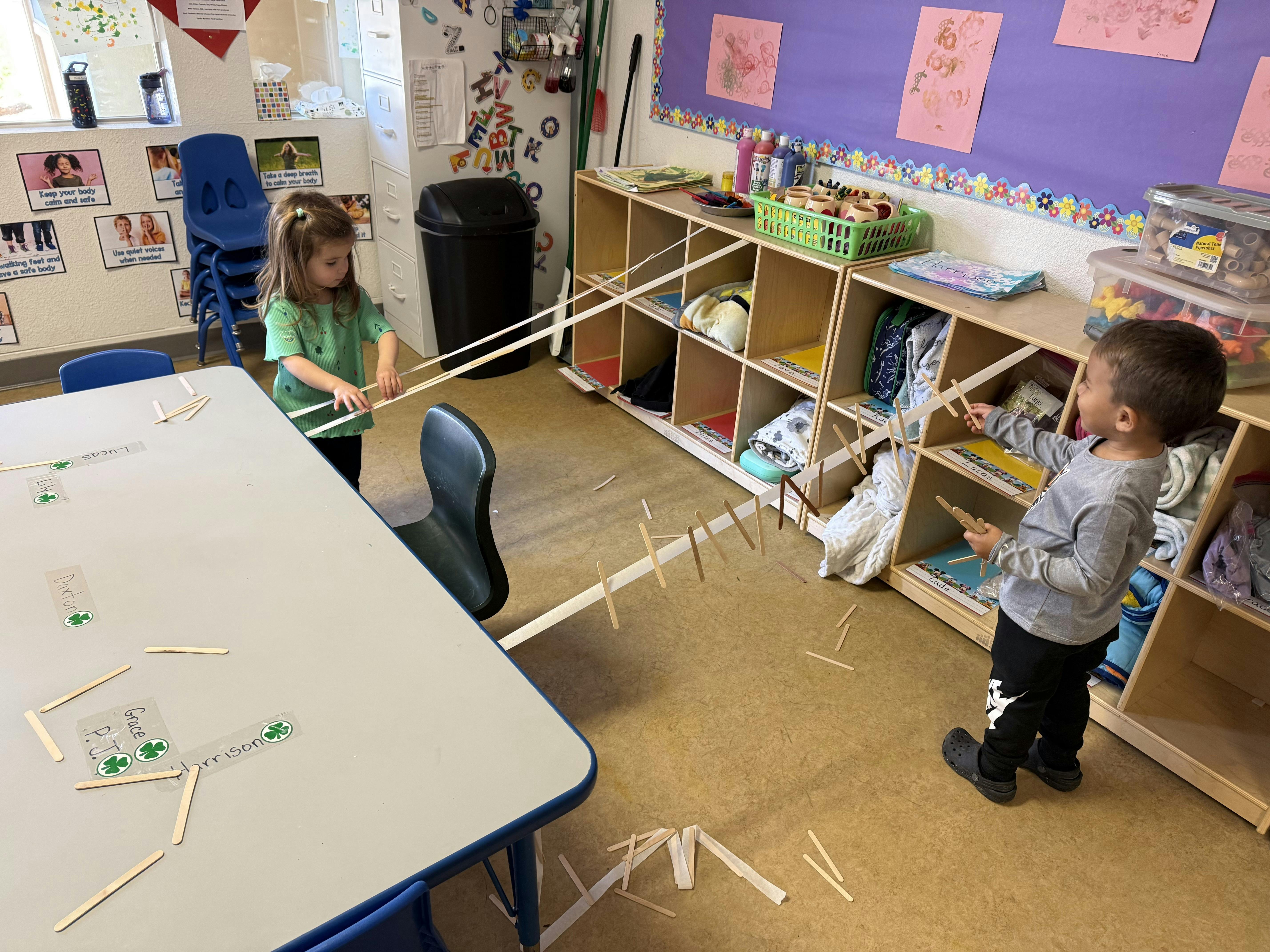 two children playing with craft sticks and tape in a classroom