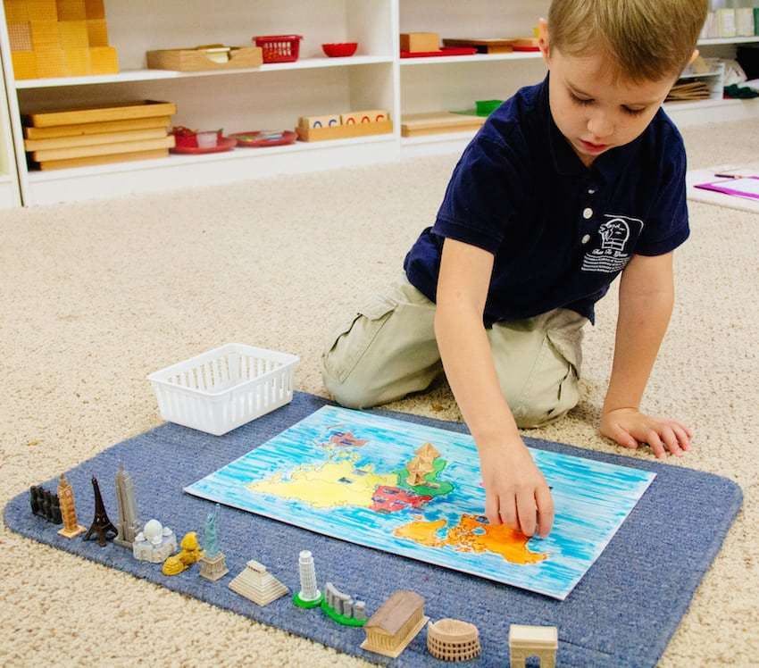 Child on floor playing with a map and small landmark models