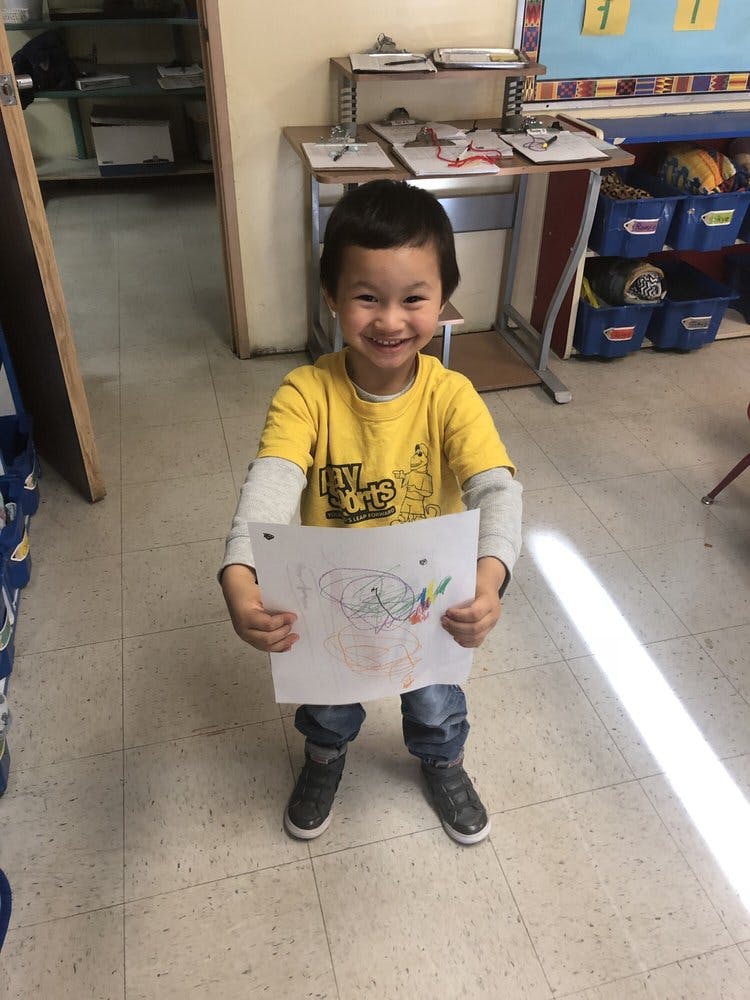 Child in a yellow shirt holding up a drawing