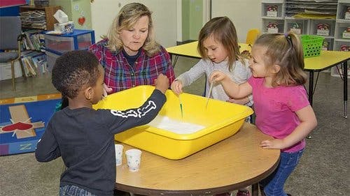 Adult and three children around a table with a yellow bin
