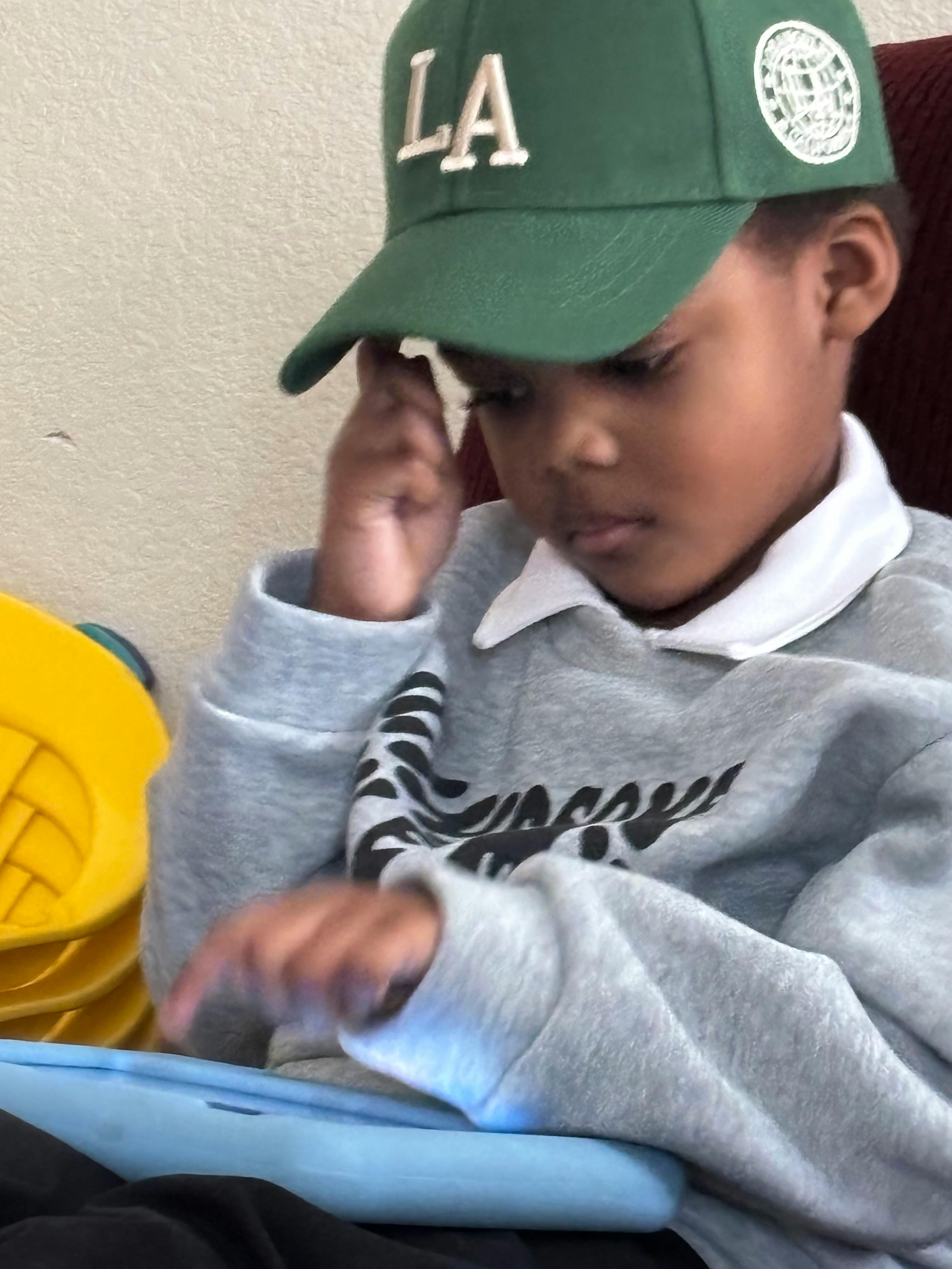 Child in a green LA hat using a tablet