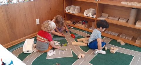 Three children playing with blocks and a road mat on the floor