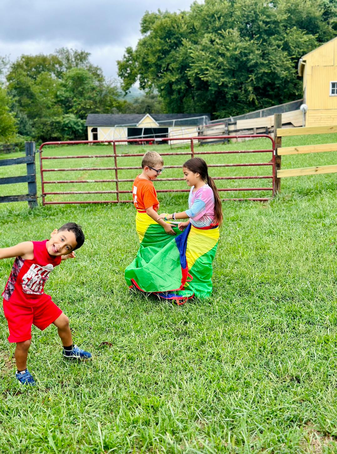 Child smiling at camera while two children are in colorful potato sacks