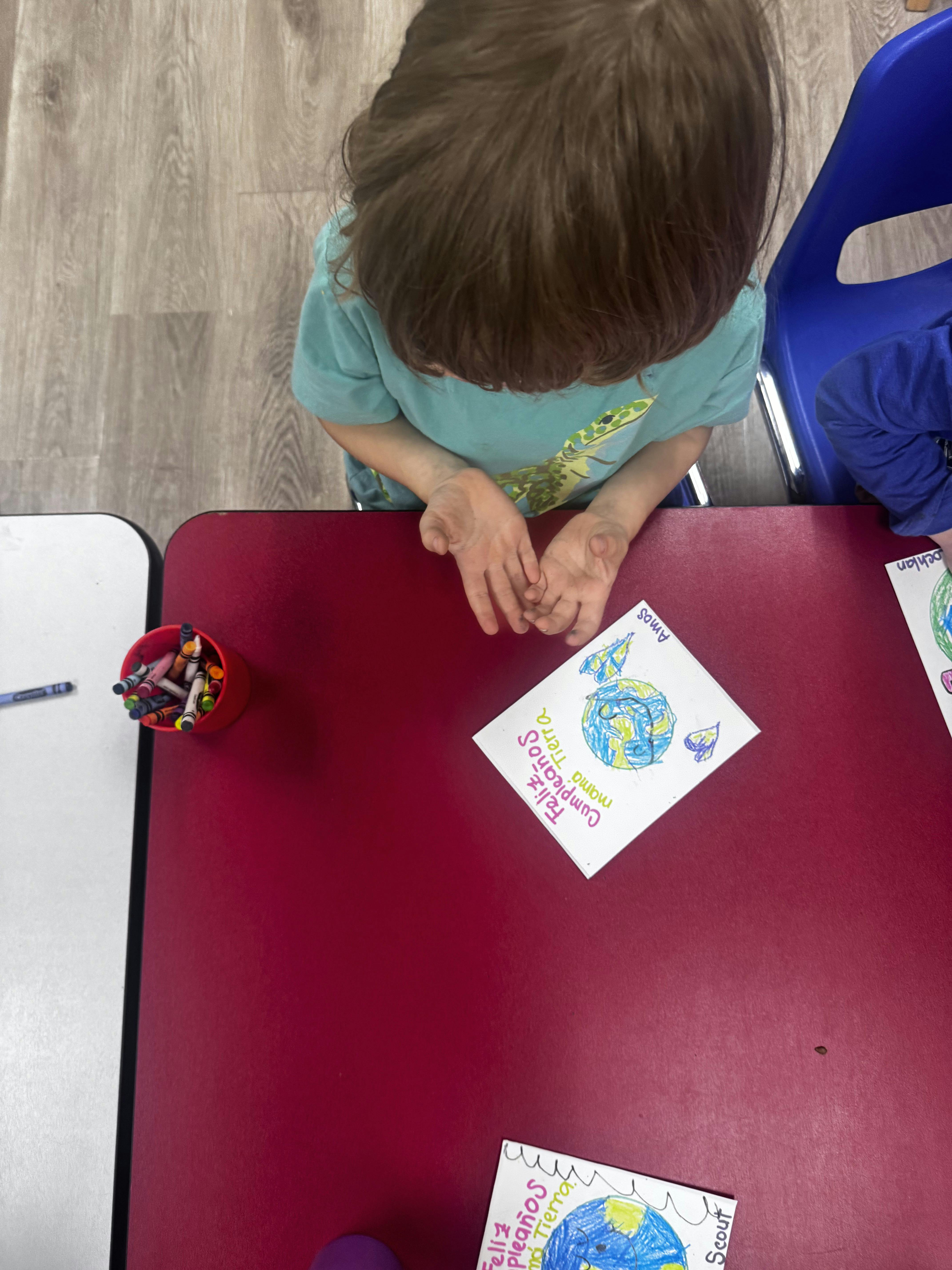 Child sitting at a red table with a drawing of the Earth