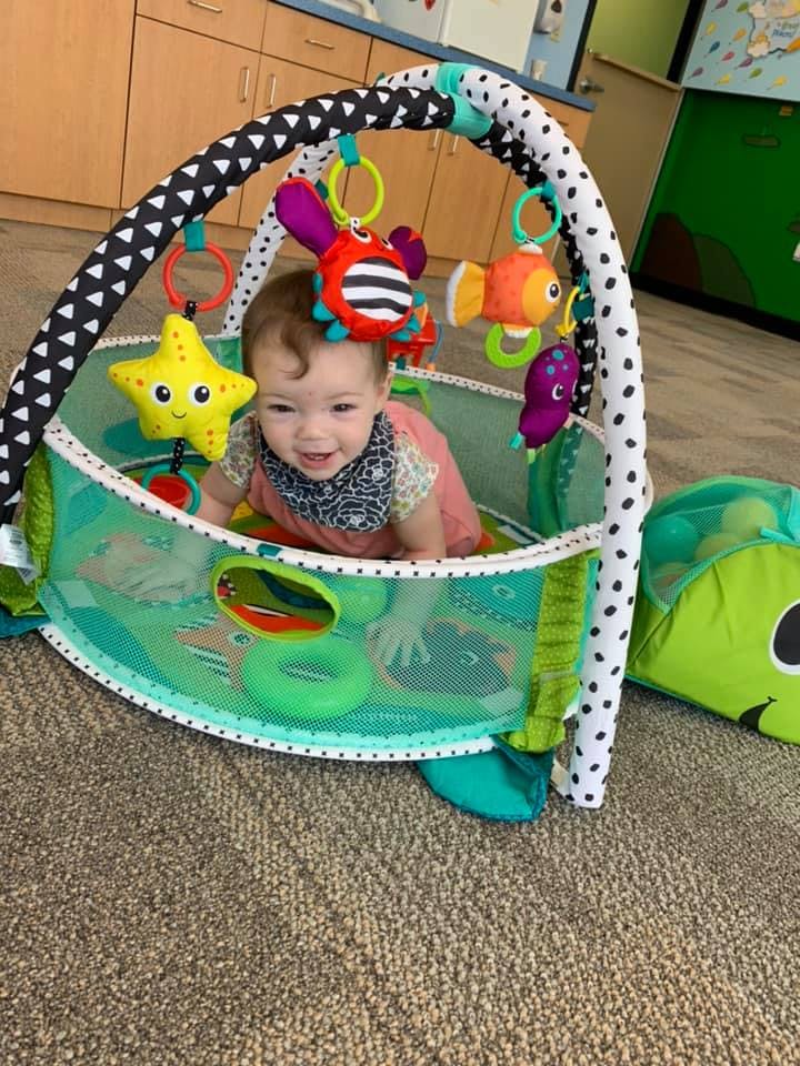 Child in a playpen with hanging toys