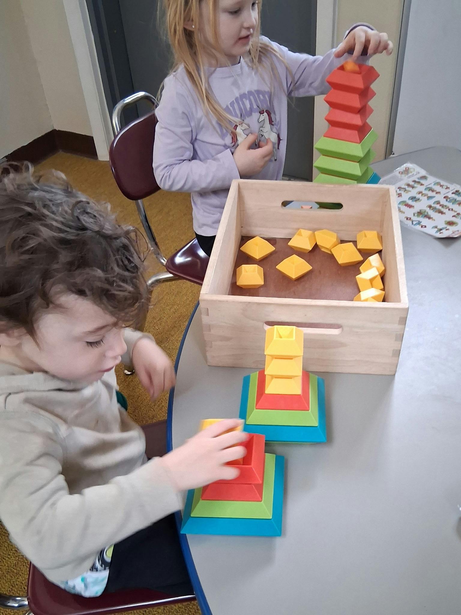 Two children playing with colorful stacking block toys at a table