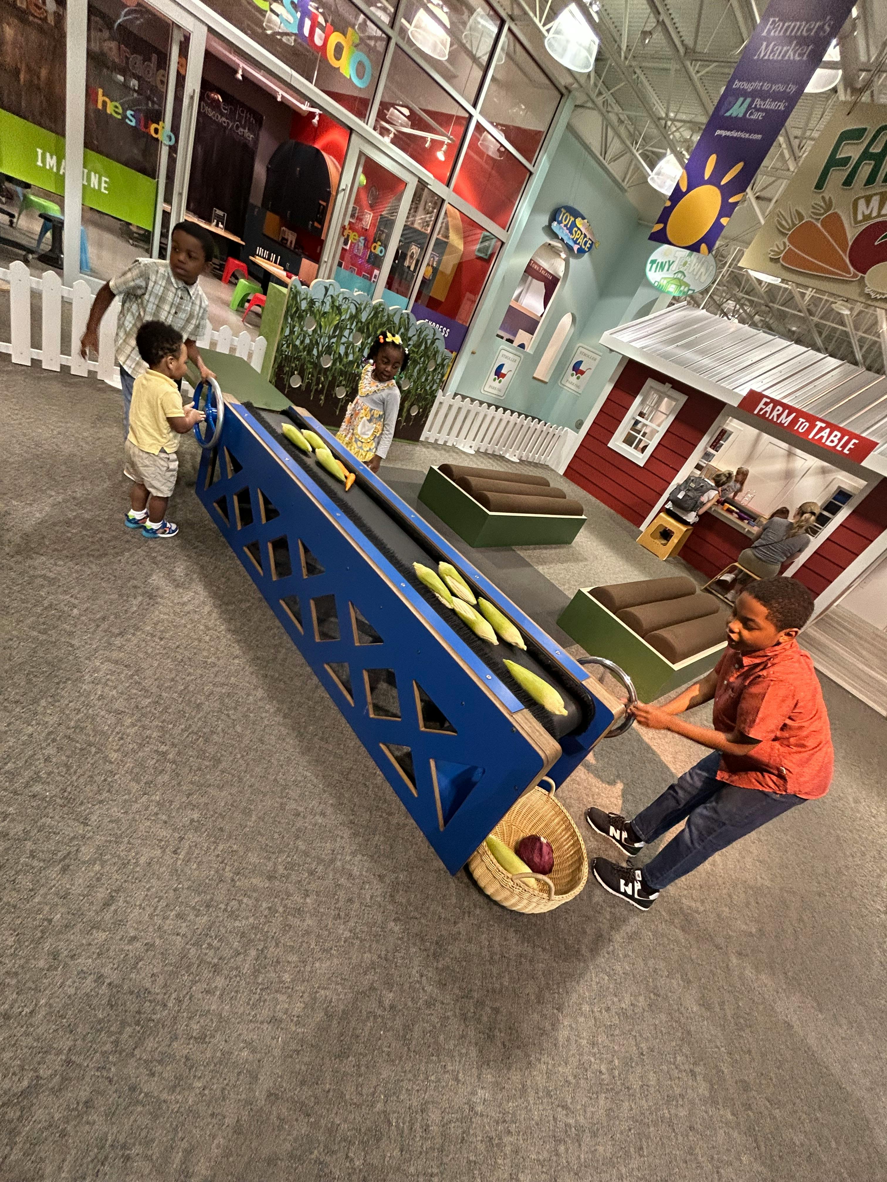 Children playing with a blue conveyor belt toy with corn cobs