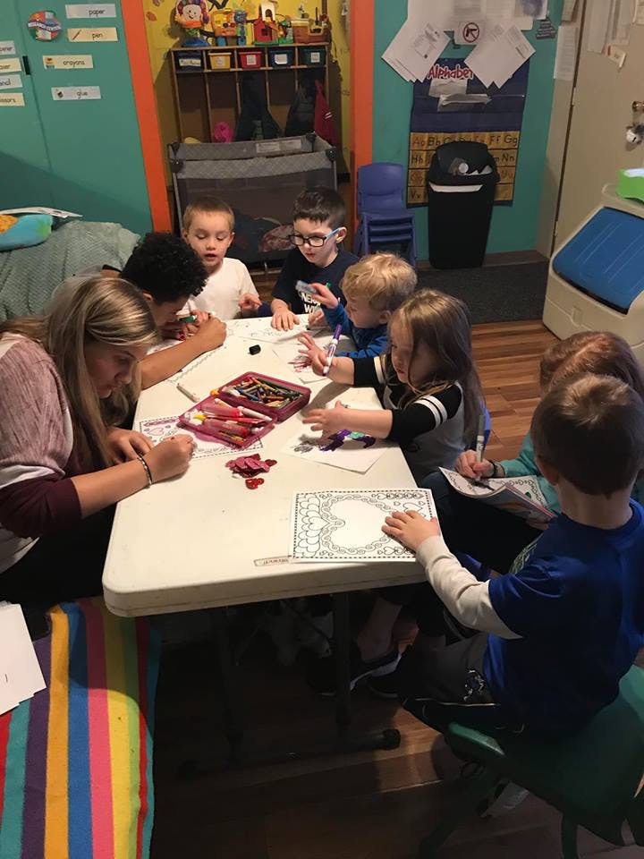 Adult and children drawing and coloring at a table in a classroom