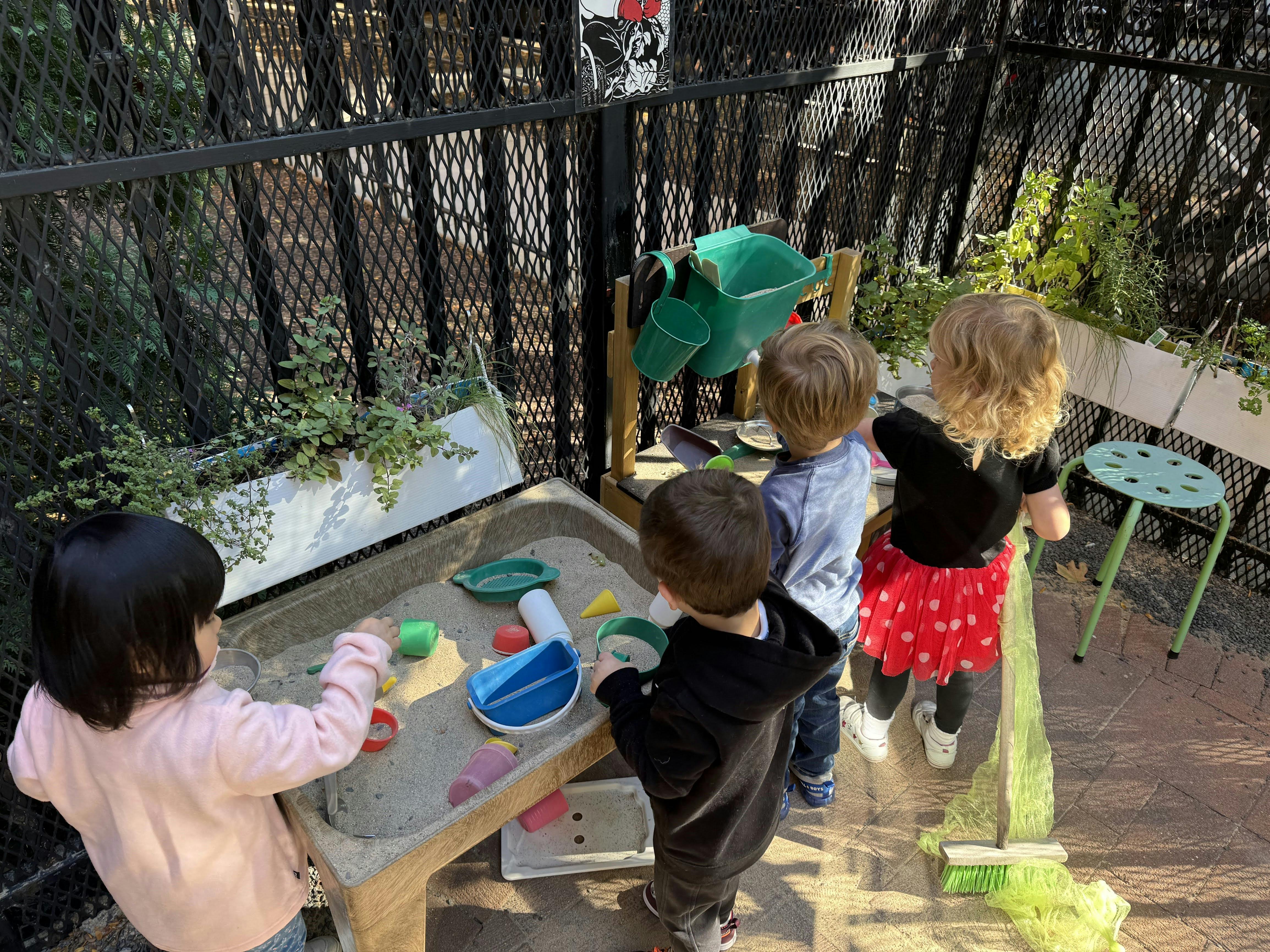 Four children playing with sand and toys at a sand table outdoors