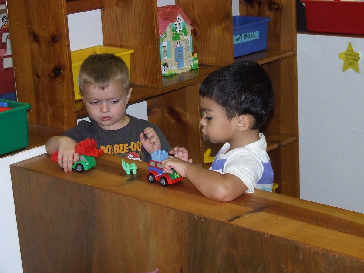 Two children playing with toy cars on a wooden surface