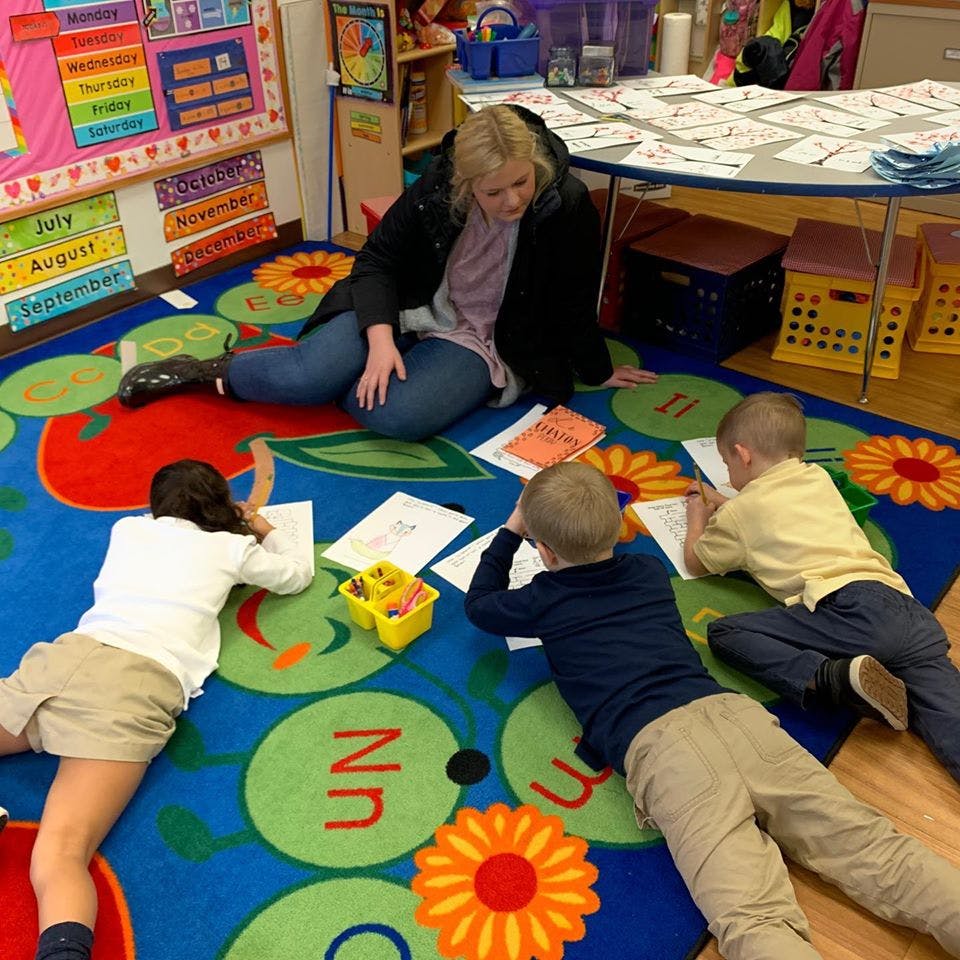 Adult and three children lying on a rug, writing on papers