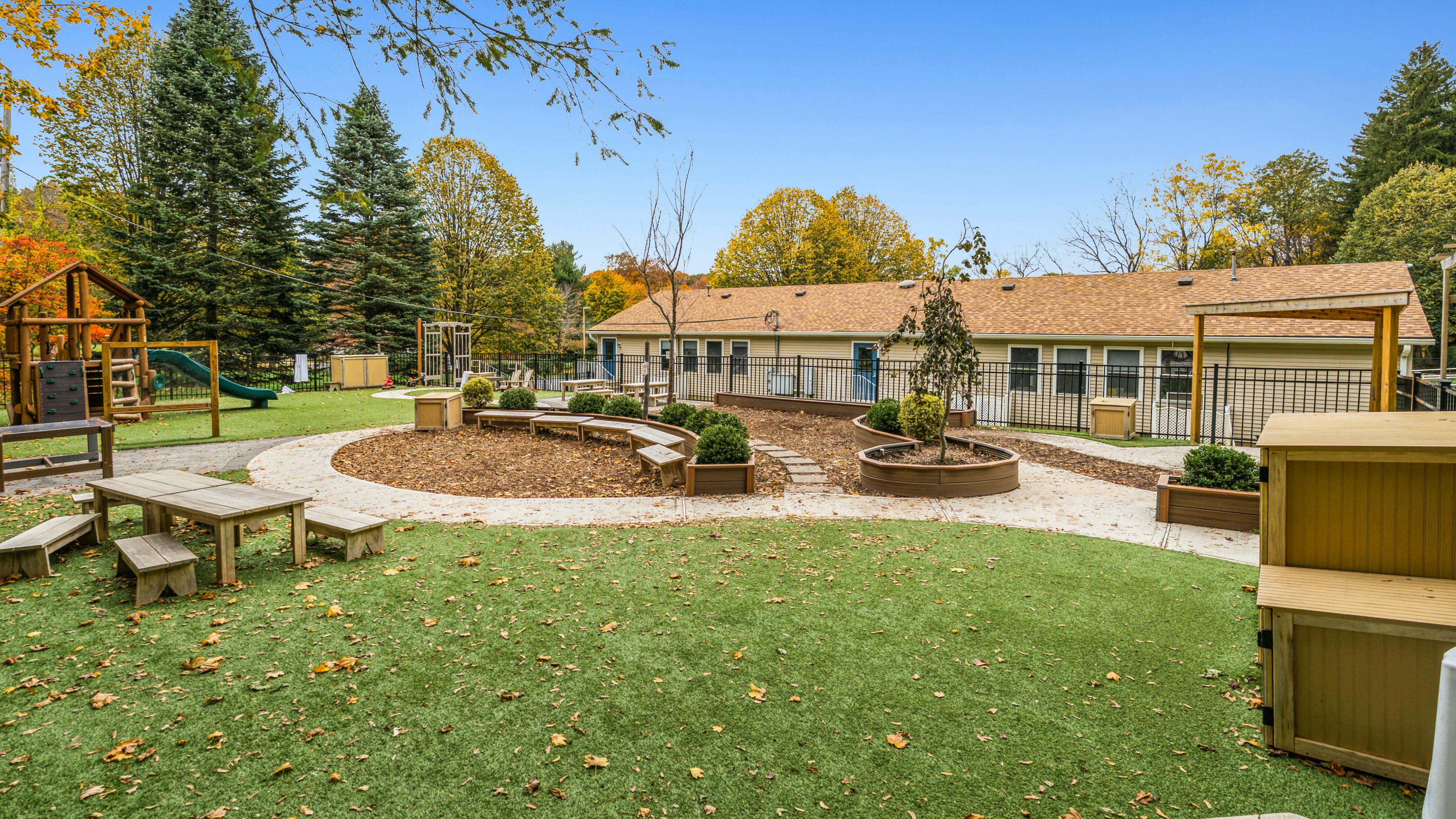Outdoor playground with artificial turf, wooden play structures, and a building