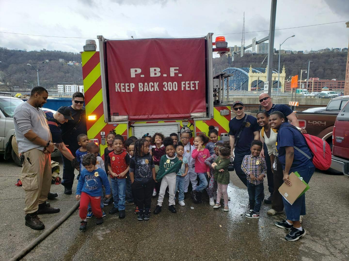 Adults and children standing in front of a fire truck with a red banner