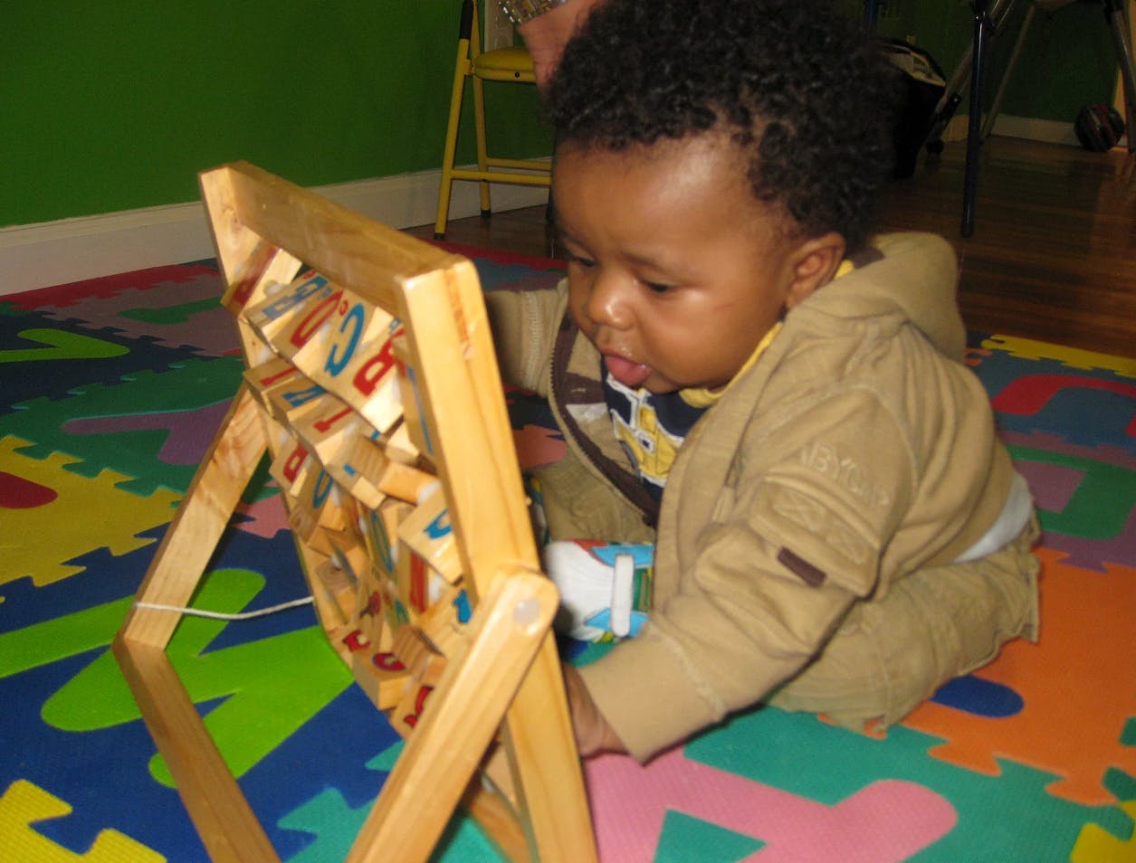 Child playing with a wooden block toy on a colorful mat
