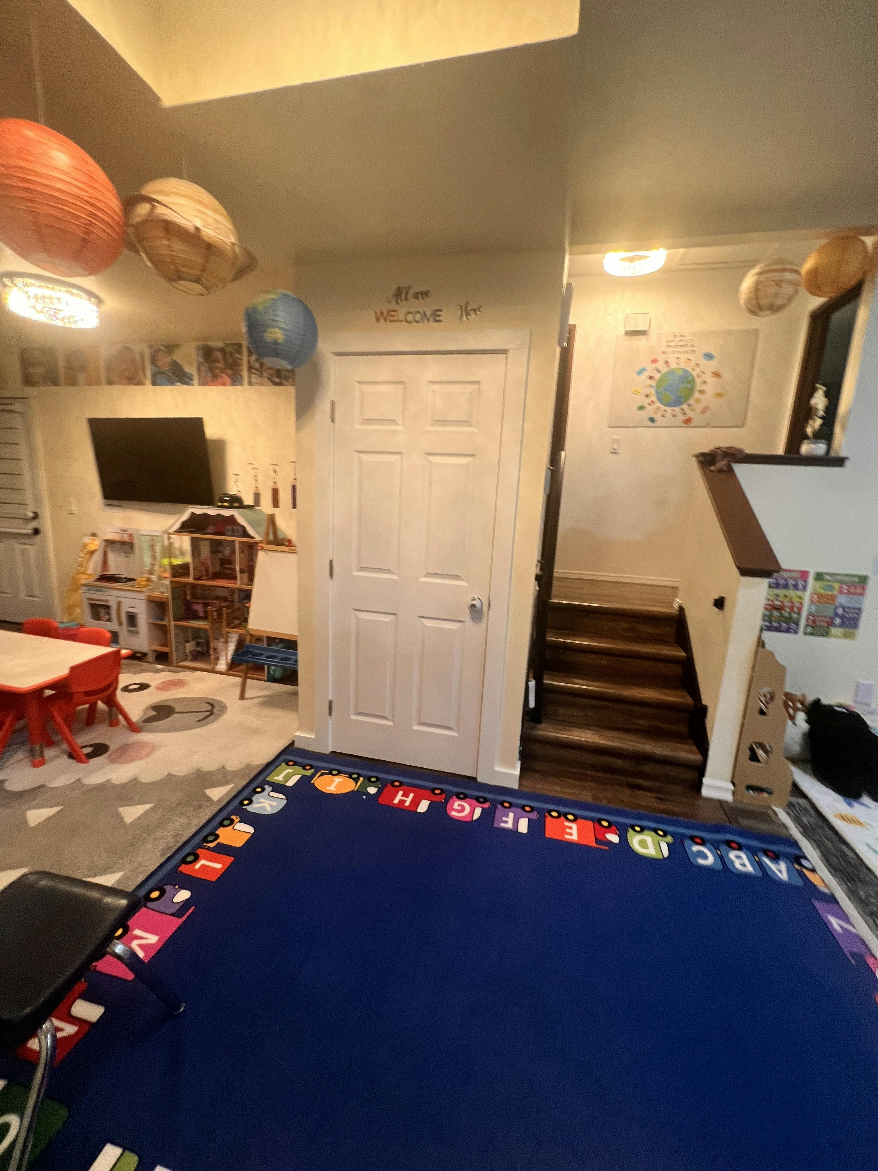 Playroom with a blue alphabet rug, toys, and a sign saying All are welcome here