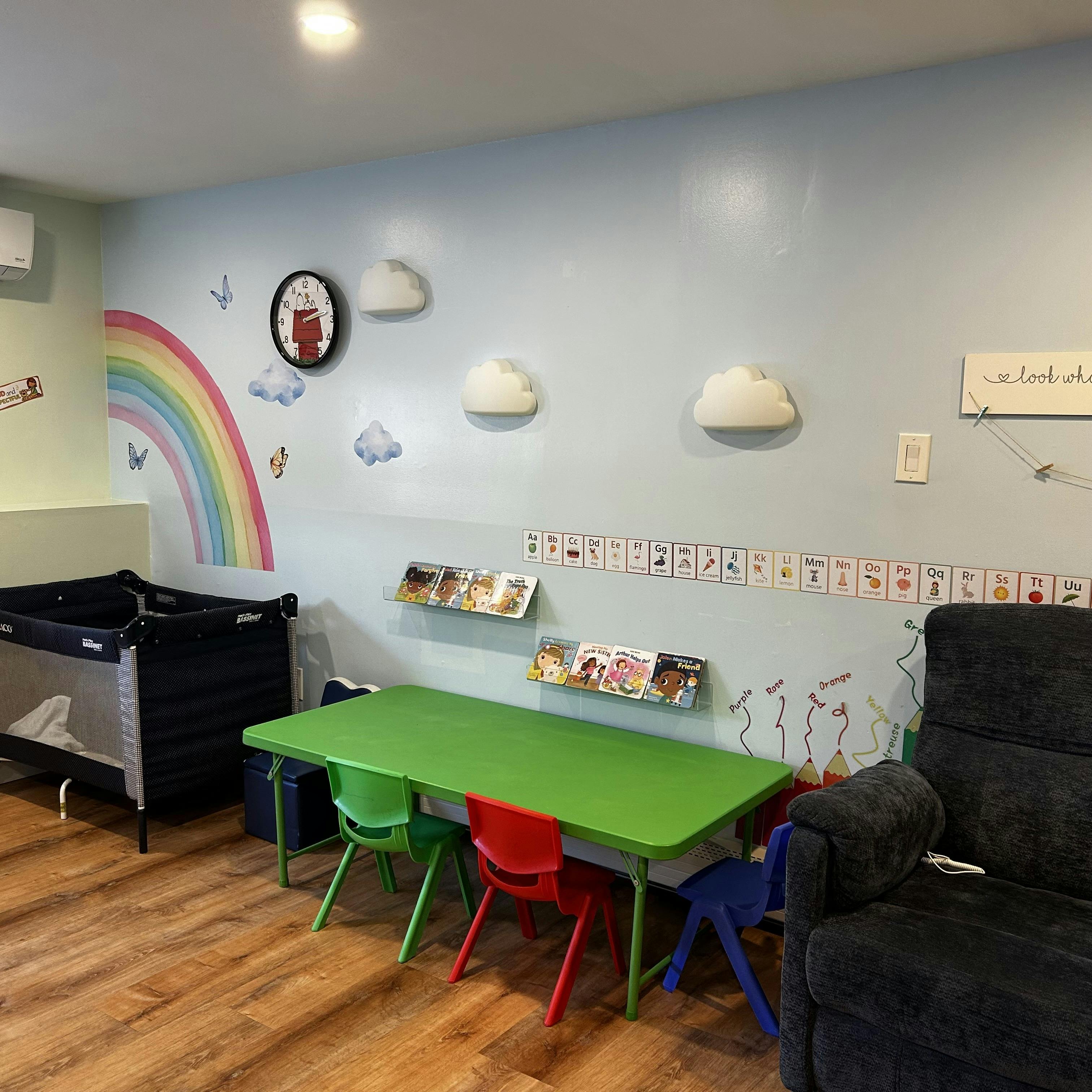 Children's playroom with a green table, small colorful chairs, books, and a crib