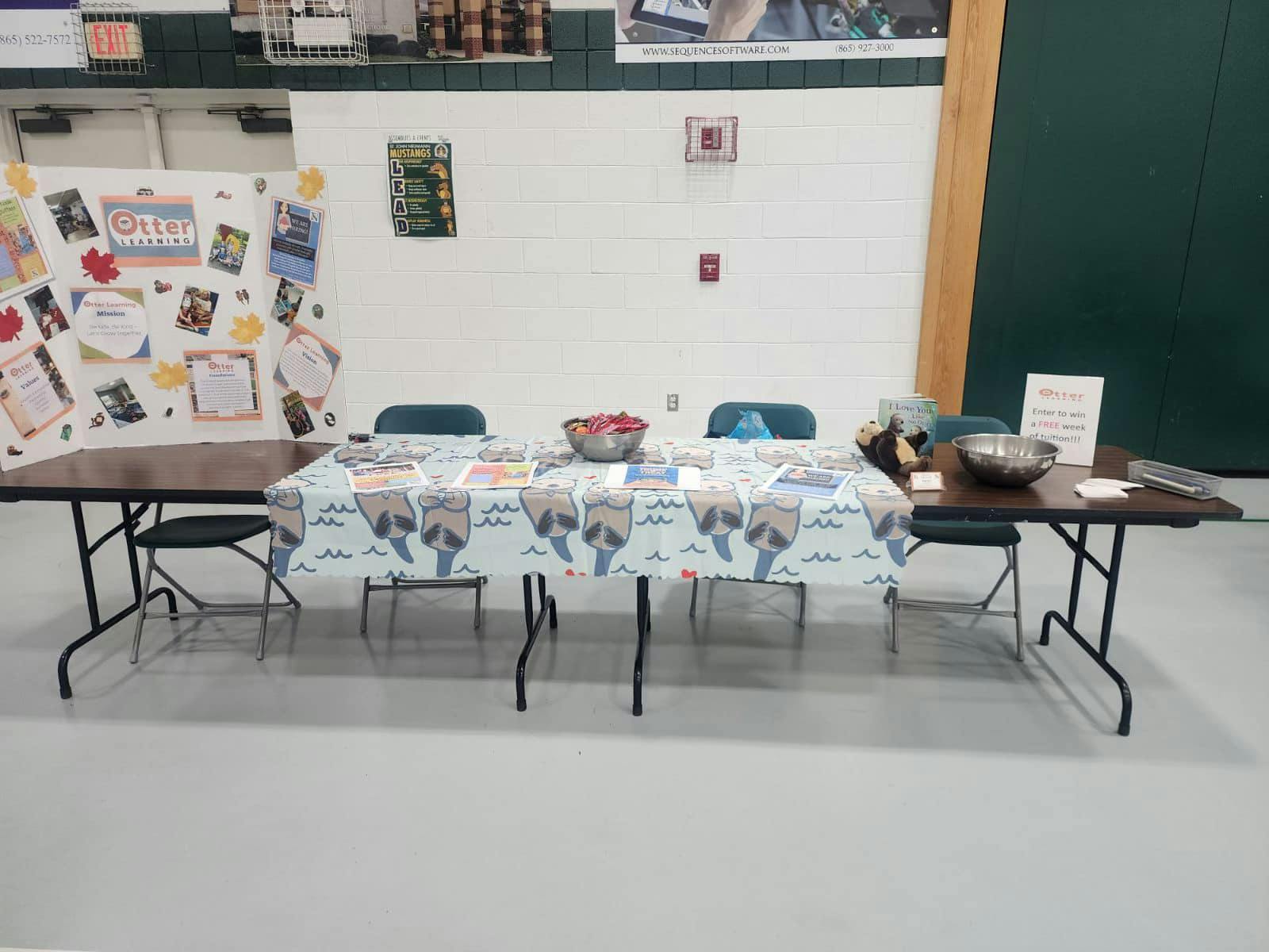 A table covered with an Otter Learning tablecloth and display boards with otter-themed graphics
