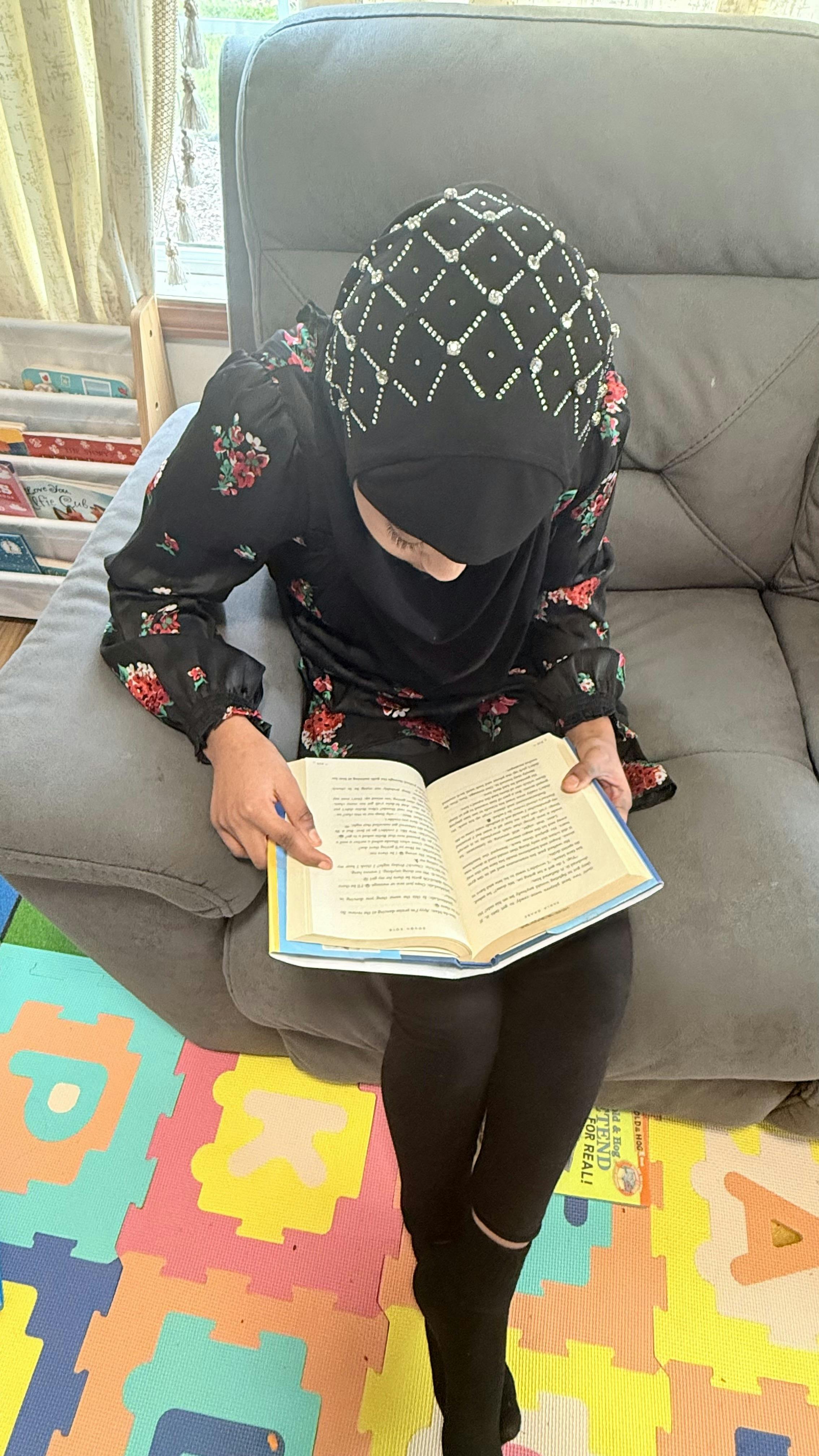Person in a patterned head covering reading a book while sitting on a couch