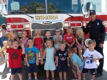 Person in uniform with a group of children in front of a fire truck