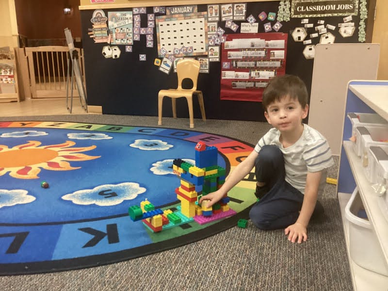Child kneeling on a rug, playing with colorful building blocks in a classroom