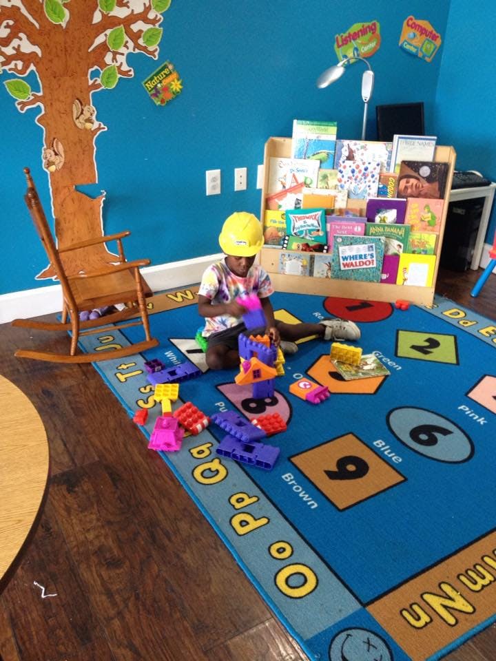 Child in a yellow hard hat playing with colorful blocks on a blue rug