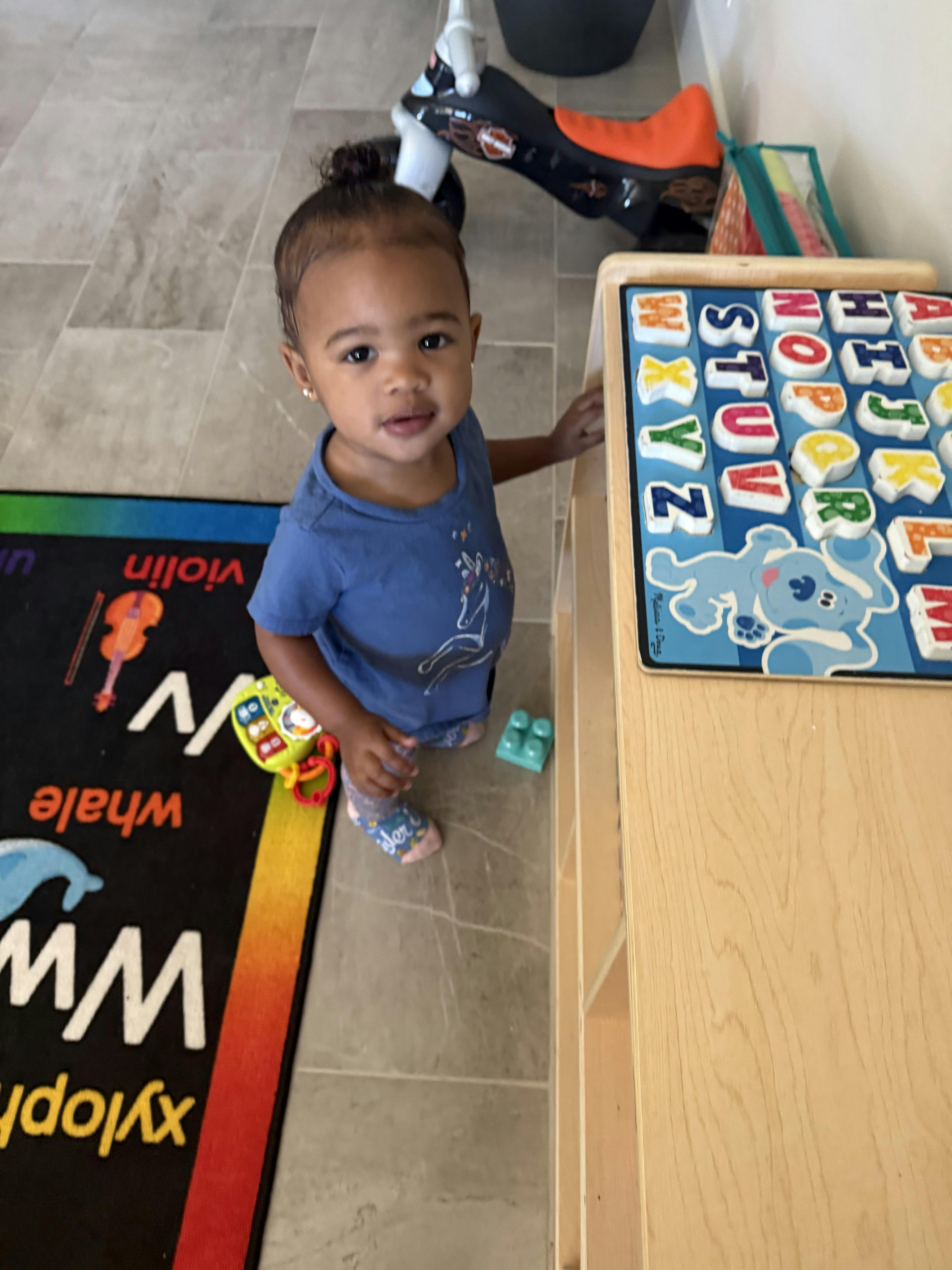 Child standing next to an alphabet puzzle board, numbers, and shapes puzzle