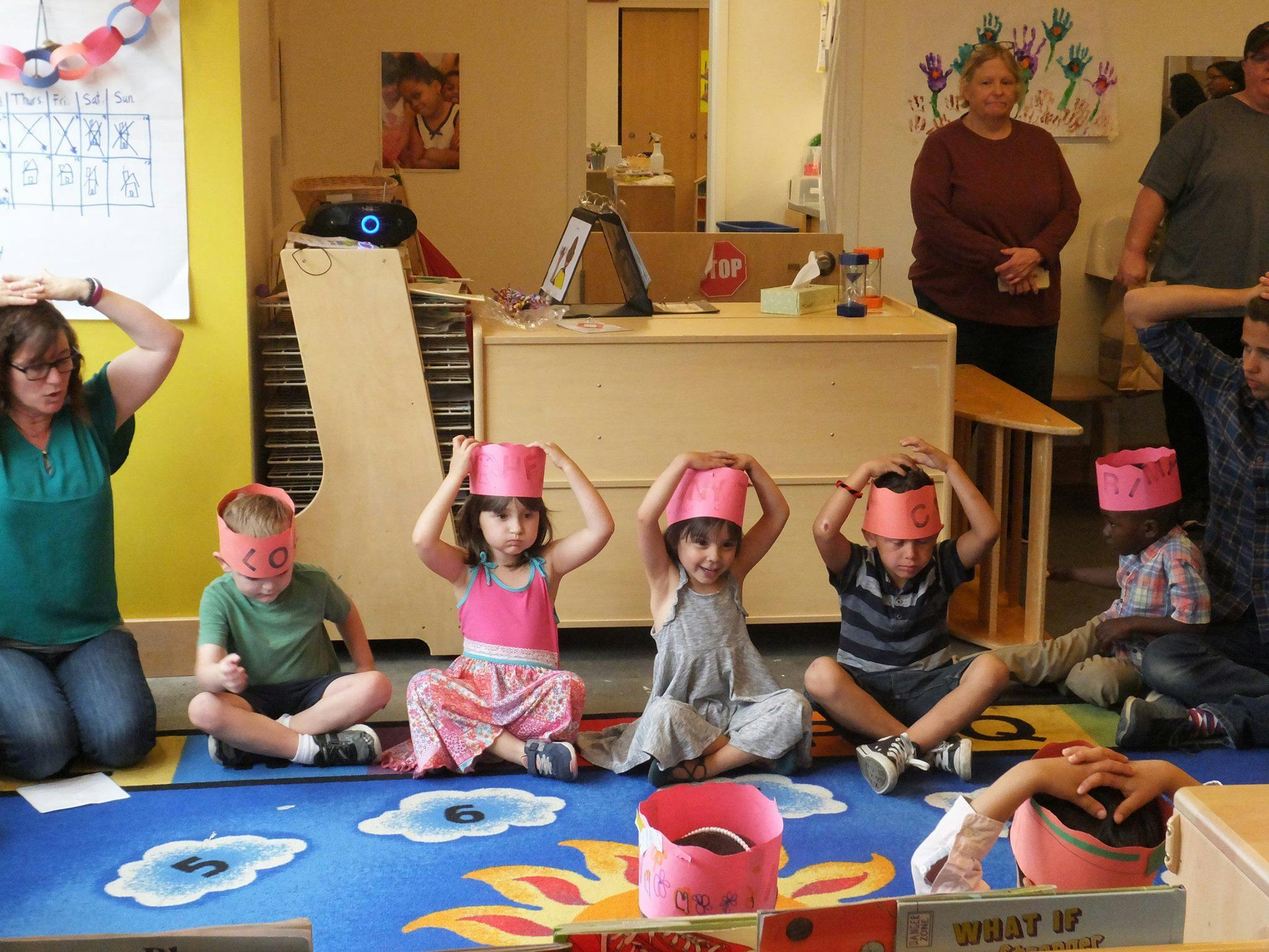 Adults and children sitting on a rug with paper hats on their heads