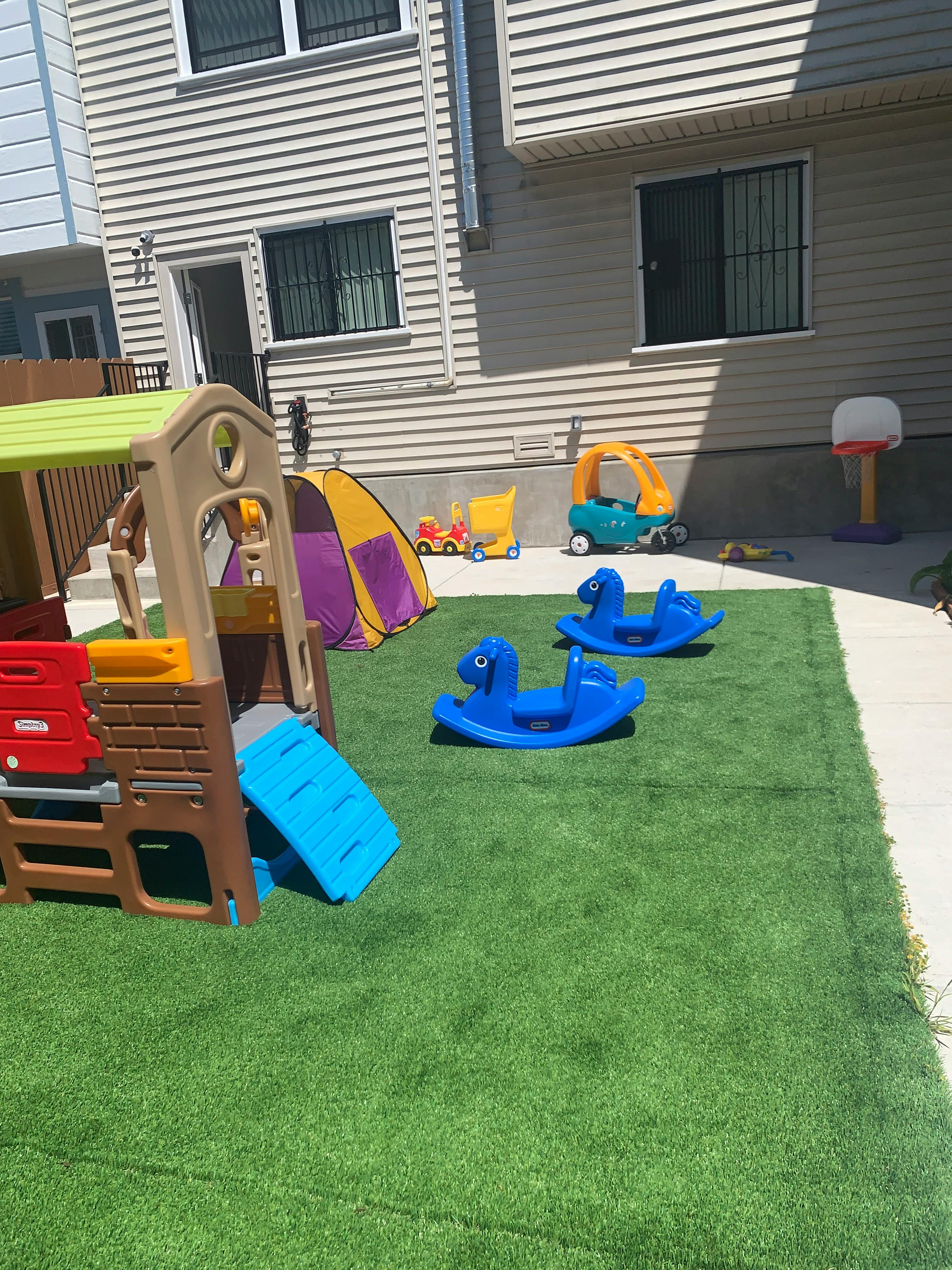 Playground with a slide, tent, and two blue rocking horses on artificial grass