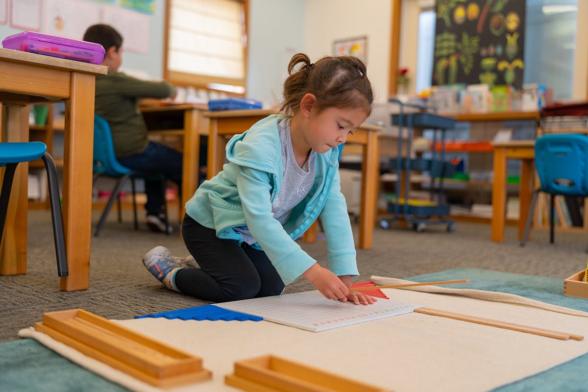 Child kneeling on floor working on paper in a classroom