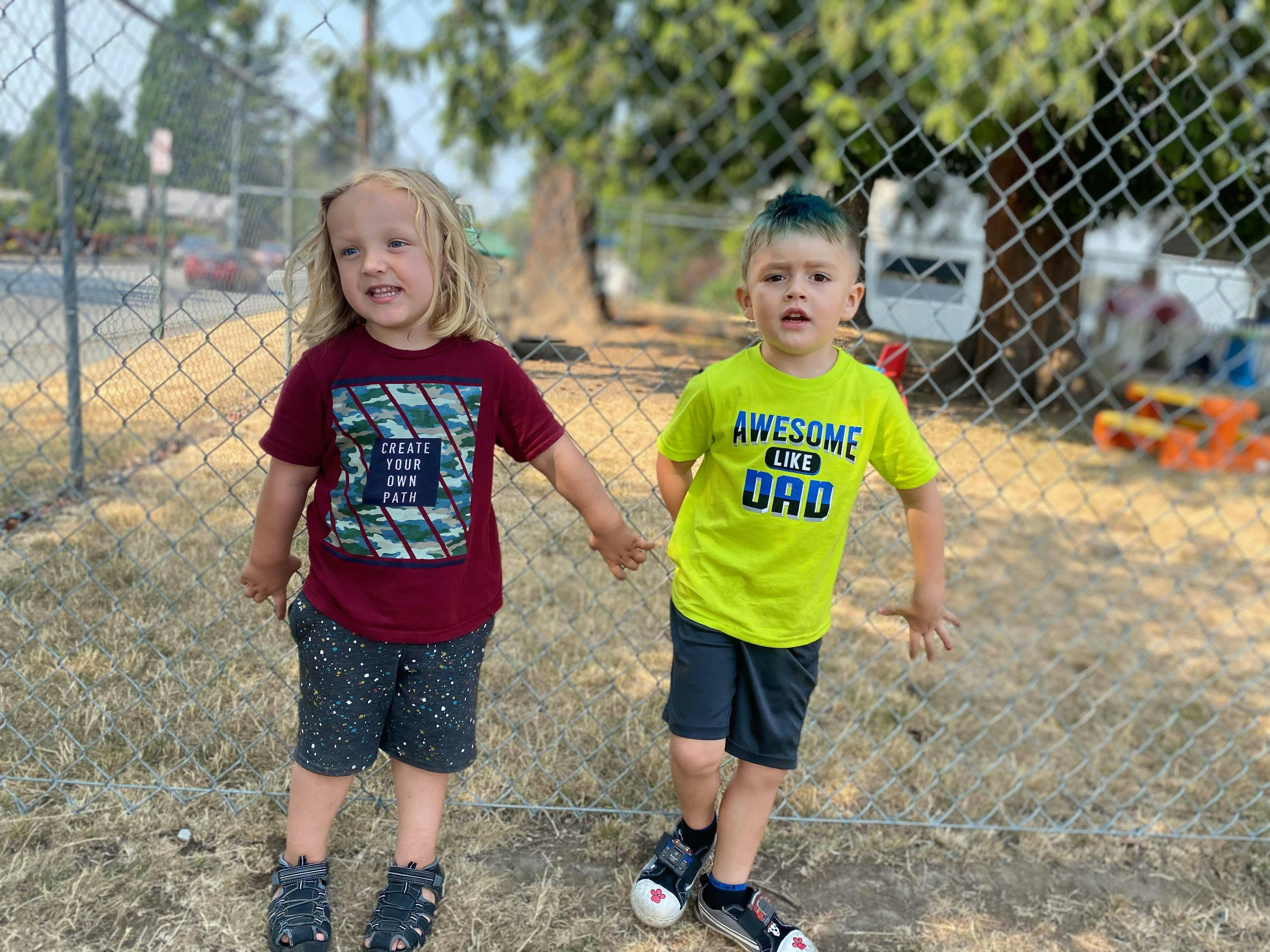 Two children standing outdoors near a fence