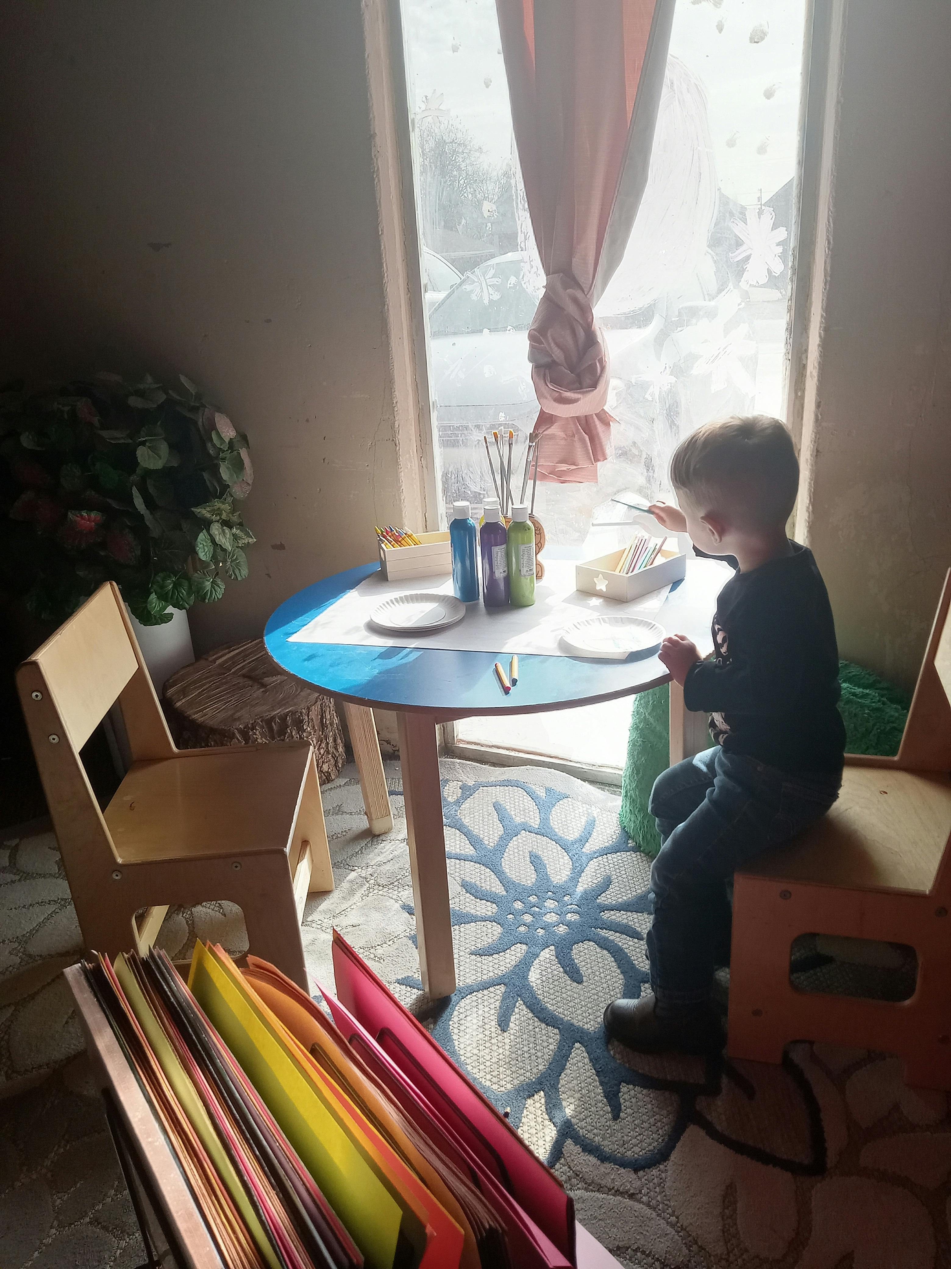 Child painting on a window from a small table