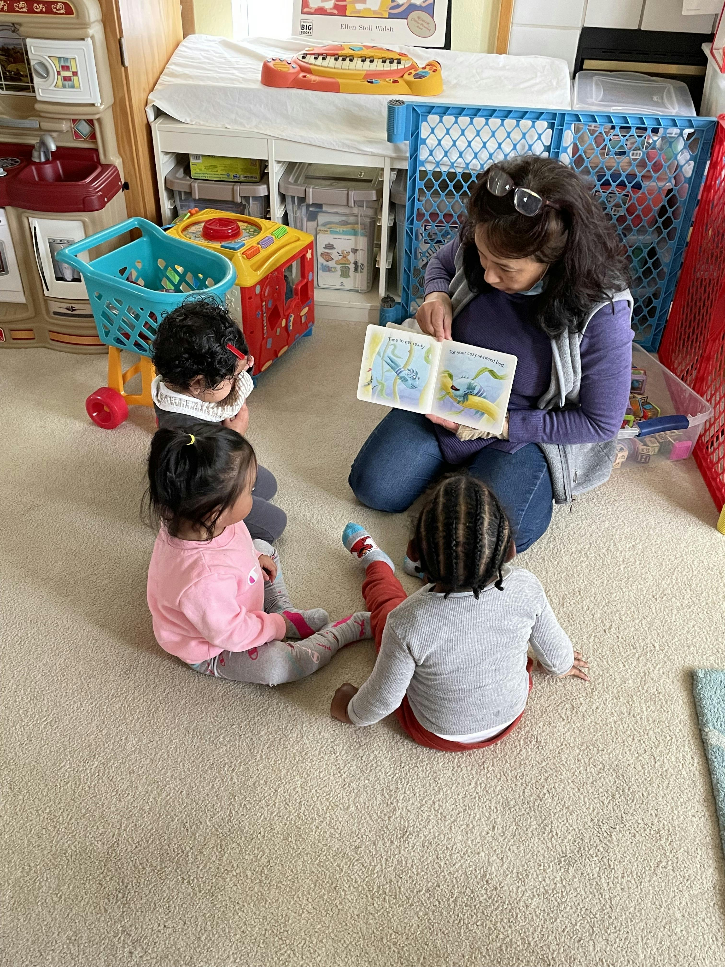Person reading a book to three children sitting on the floor