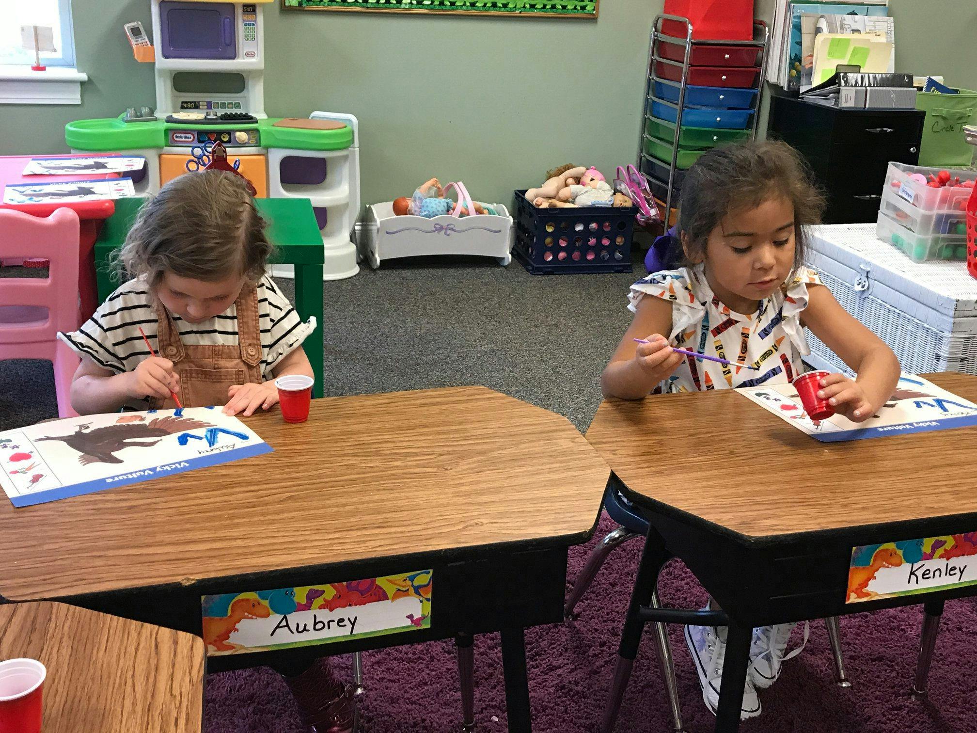 Two children painting at desks in a classroom