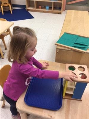 Child playing with a shape sorter toy in a classroom