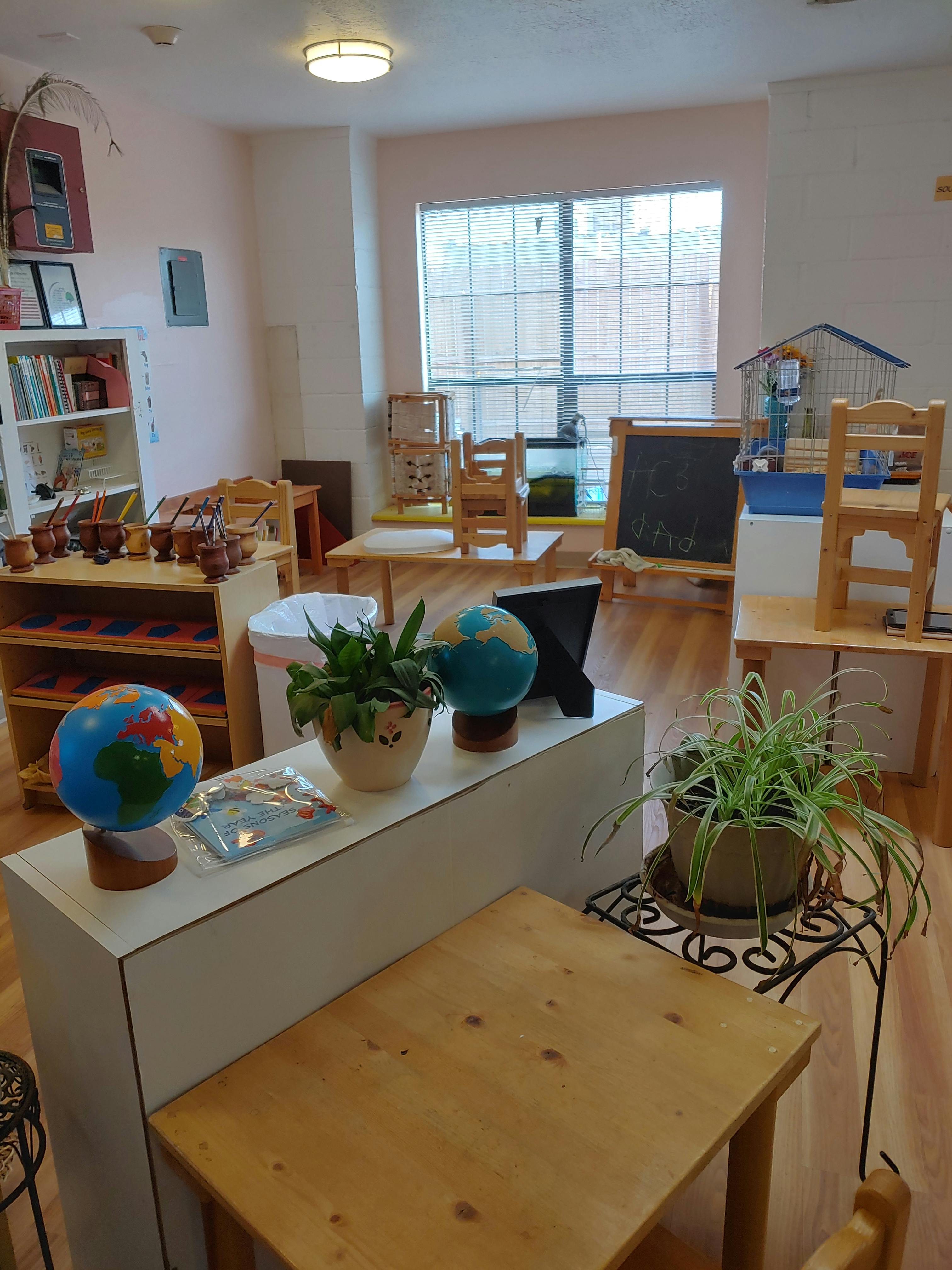 Classroom with small wooden furniture, globes, and plants