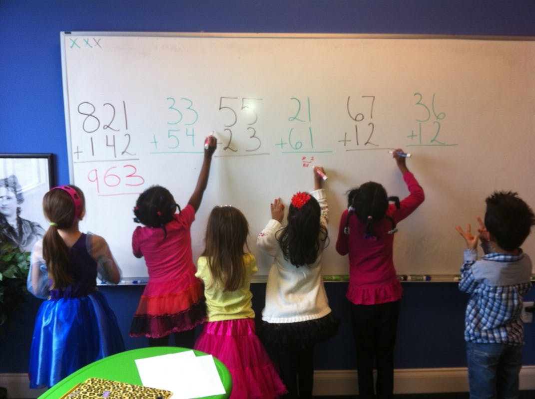 Children writing math problems on a whiteboard in a classroom