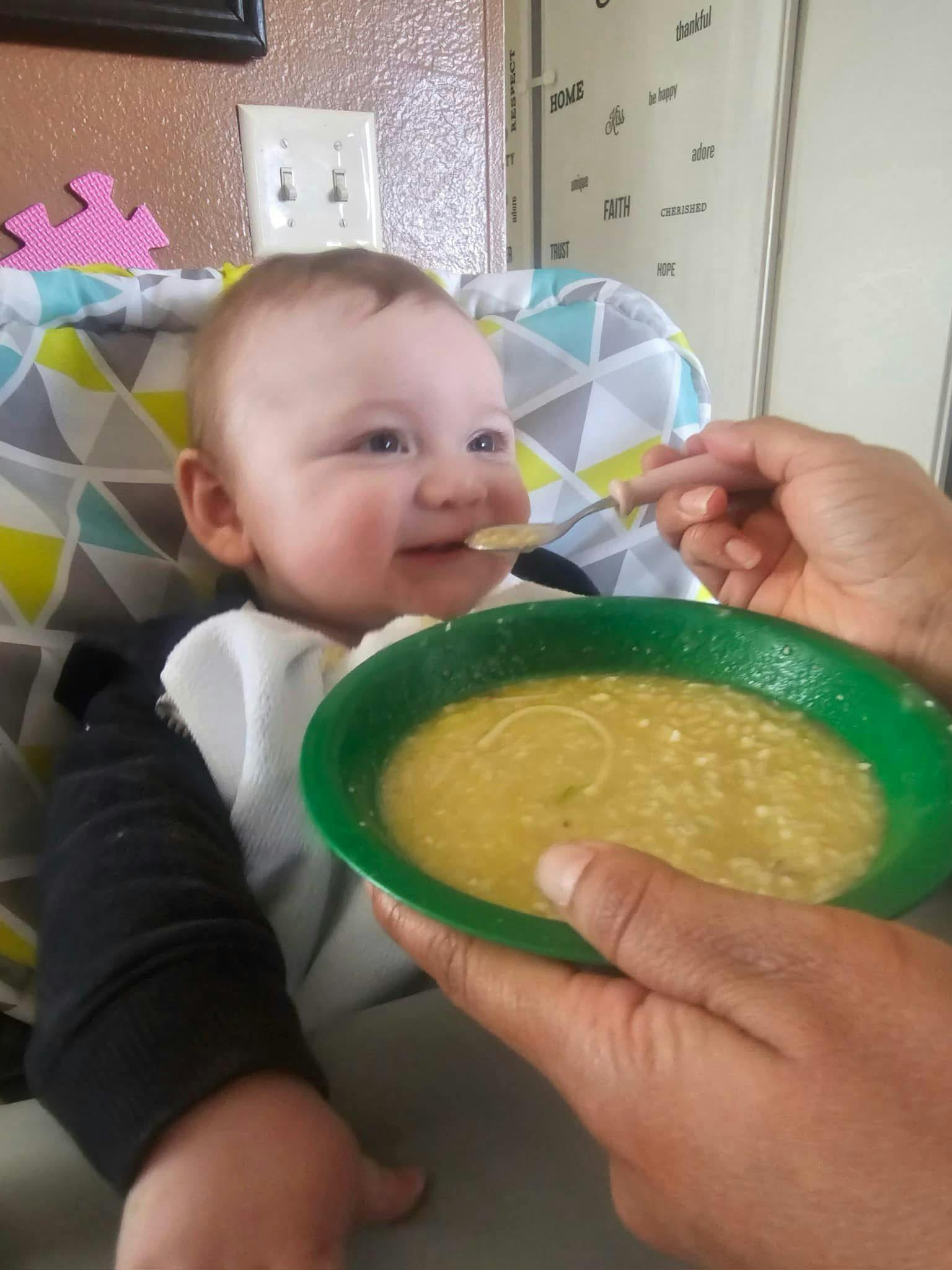 Child in high chair being fed from a green bowl