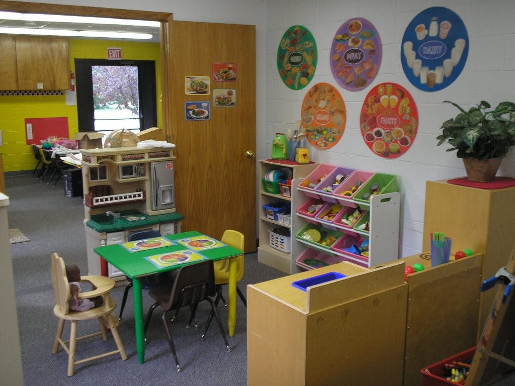 Playroom with small green table and chairs, toy kitchen, and storage shelves