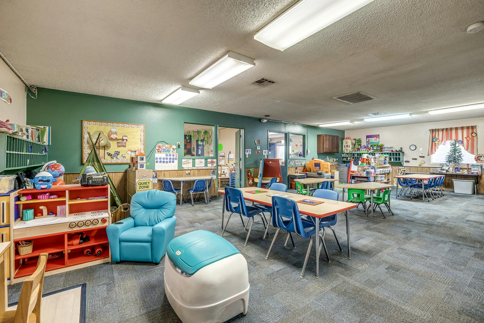 Classroom with small tables and chairs, a blue armchair, and shelves with shelves of toys