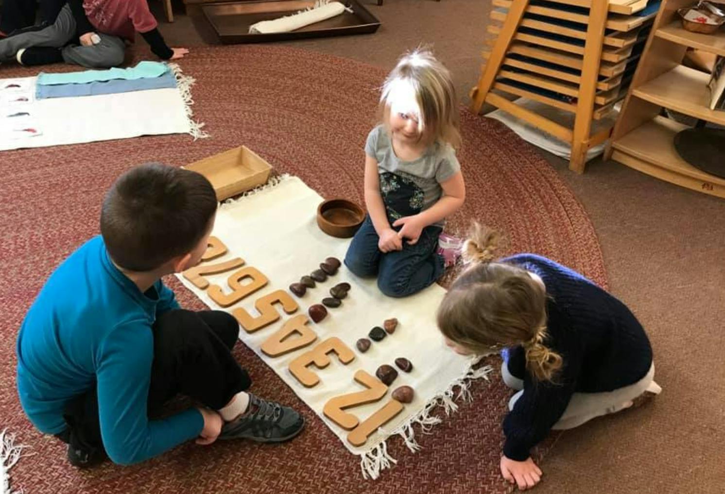 Three children on a rug playing with wooden numbers and small objects