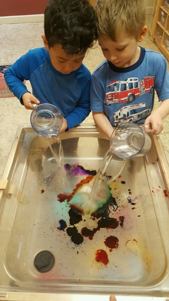 Two children pouring water into a tray with colorful liquid
